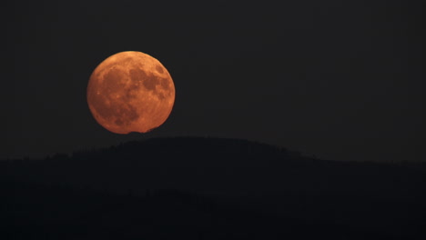 stunning full orange moon rising over mountains at night