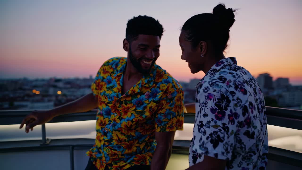 Young couple laughing and sharing a romantic moment on a rooftop at sunset, enjoying the stunning cityscape while wearing colorful Hawaiian shirts. Joyful smiles and carefree vibes fill the air