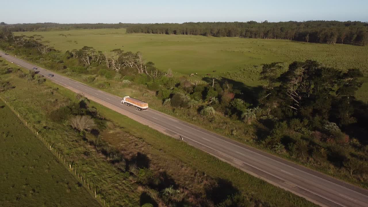 Toma aérea de seguimiento de un camión industrial transportando carga y mercancías mientras conduce por una carretera rural en Uruguay