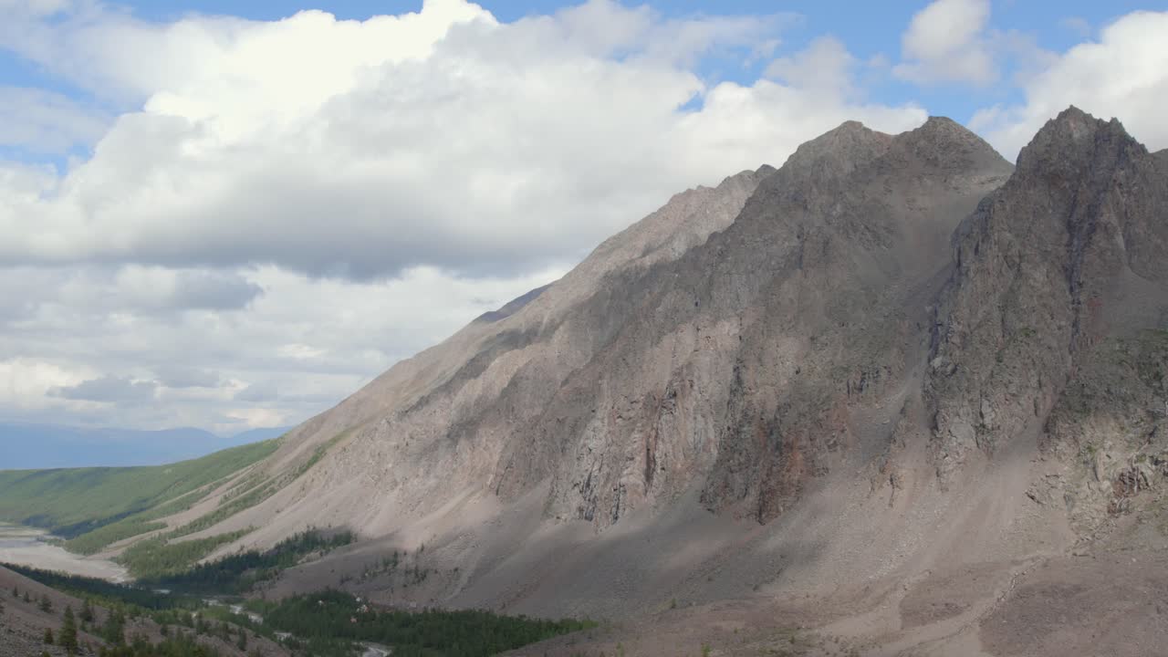 Ampia ripresa paesaggistica della Valle dell'Aktru sui Monti Altai, Russia, con cime rocciose scoscese, una valle fluviale verde e nuvole in movimento in una giornata estiva