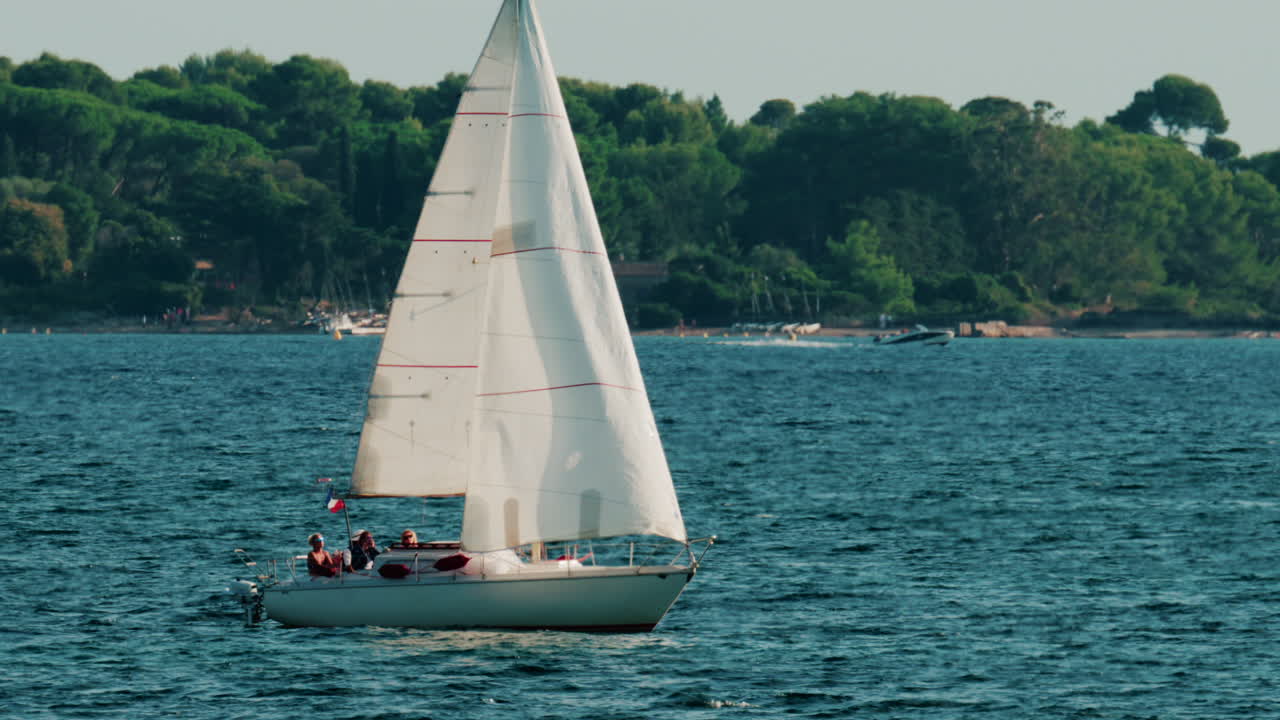 White sailboat gliding across calm blue water near a green coastline