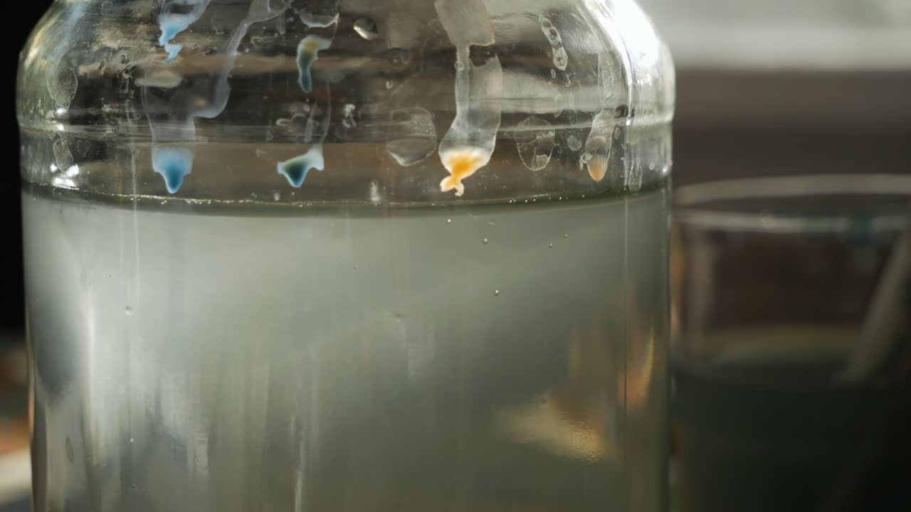 Artist dipping brush with orange paint in water, extreme close up