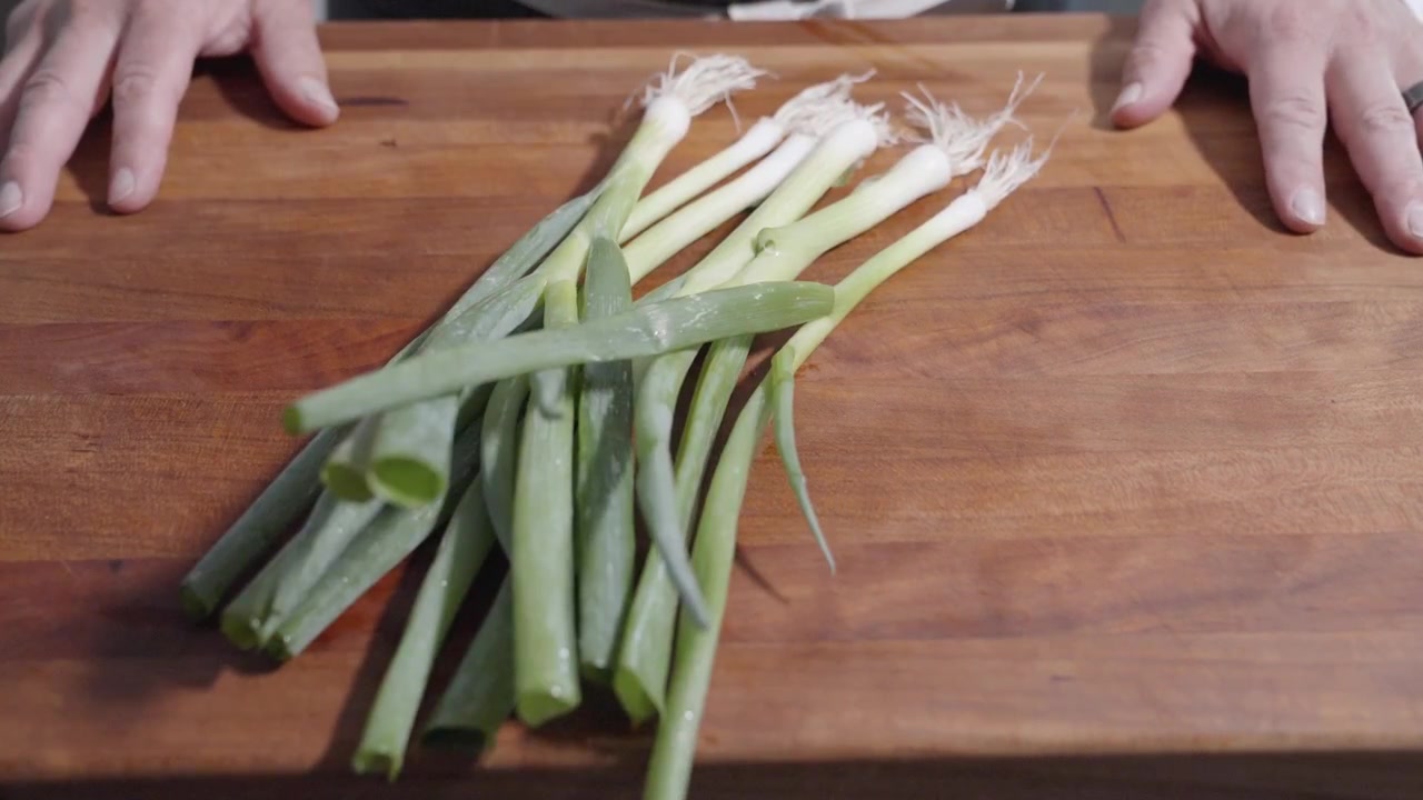 Een statisch shot toont een chef-kok die losse lente-uitjes op een snijplank gooit, klaar om te hakken. Ideaal voor kooktutorials, ingrediëntenvoorbereiding en het demonstreren van culinaire technieken