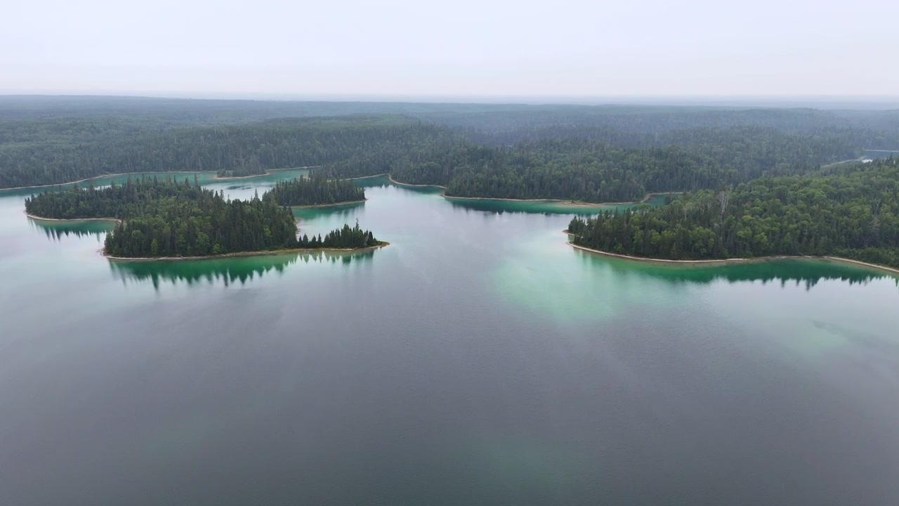 Vista aérea de um lago azul tranquilo com águas rasas esmeralda, ilhas florestadas distantes e água calma e reflexiva no Lago Arnott, no Norte de Ontário
