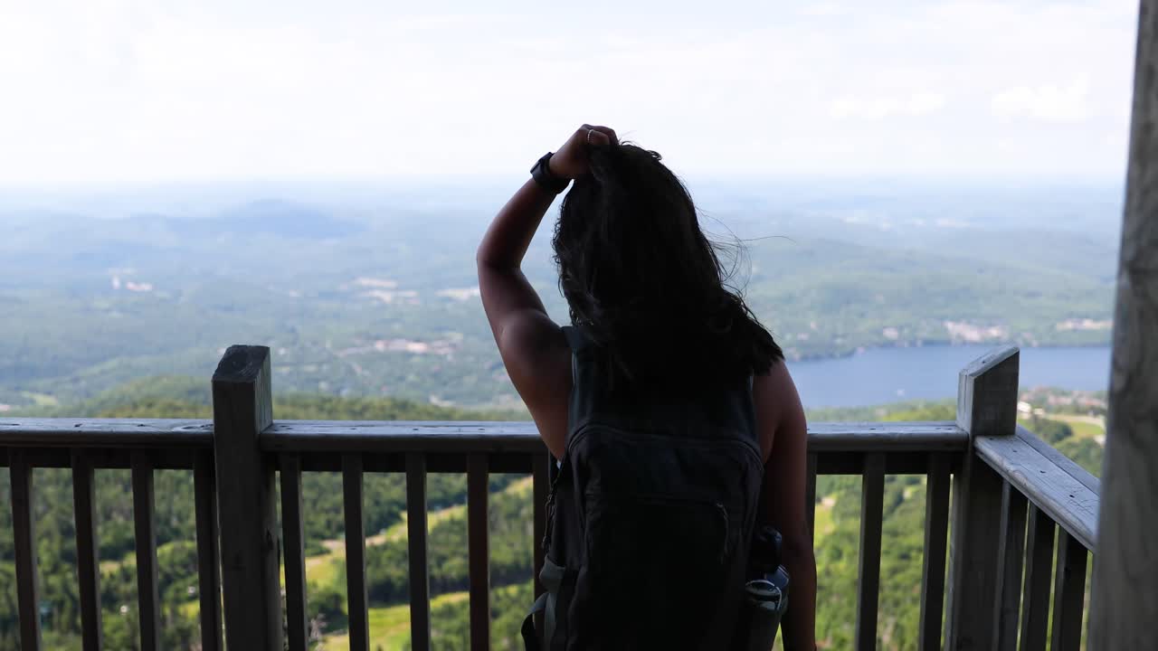 Female hiker looking at at view from the top of a mountain on a sunny summer day in Quebec