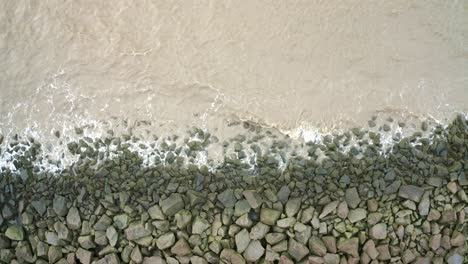 sea waves hitting rocks on a sea dyke, overhead drone shot descending