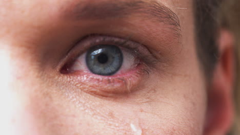 extreme close up of eye as unhappy man cries into camera in studio