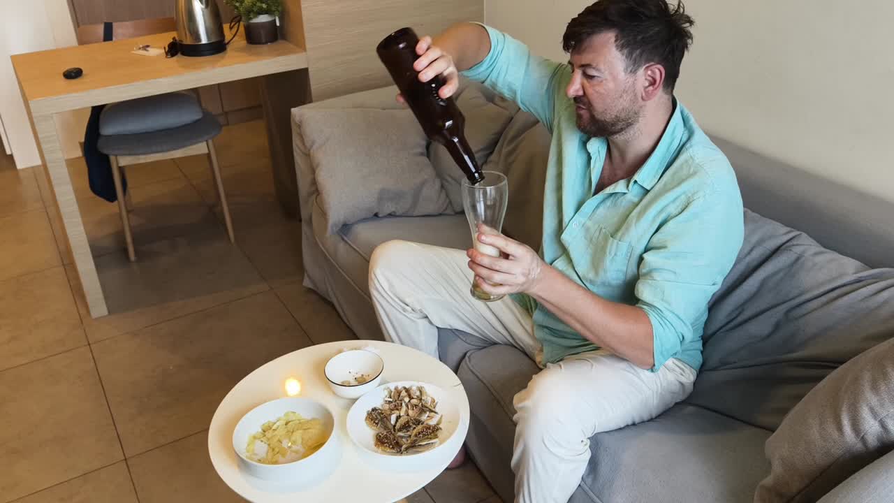 Man eating snacks and drinking beer on a couch in his living room