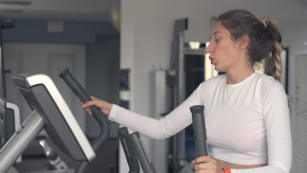 Donna in abbigliamento sportivo bianco che si allena sulla macchina ellittica in palestra