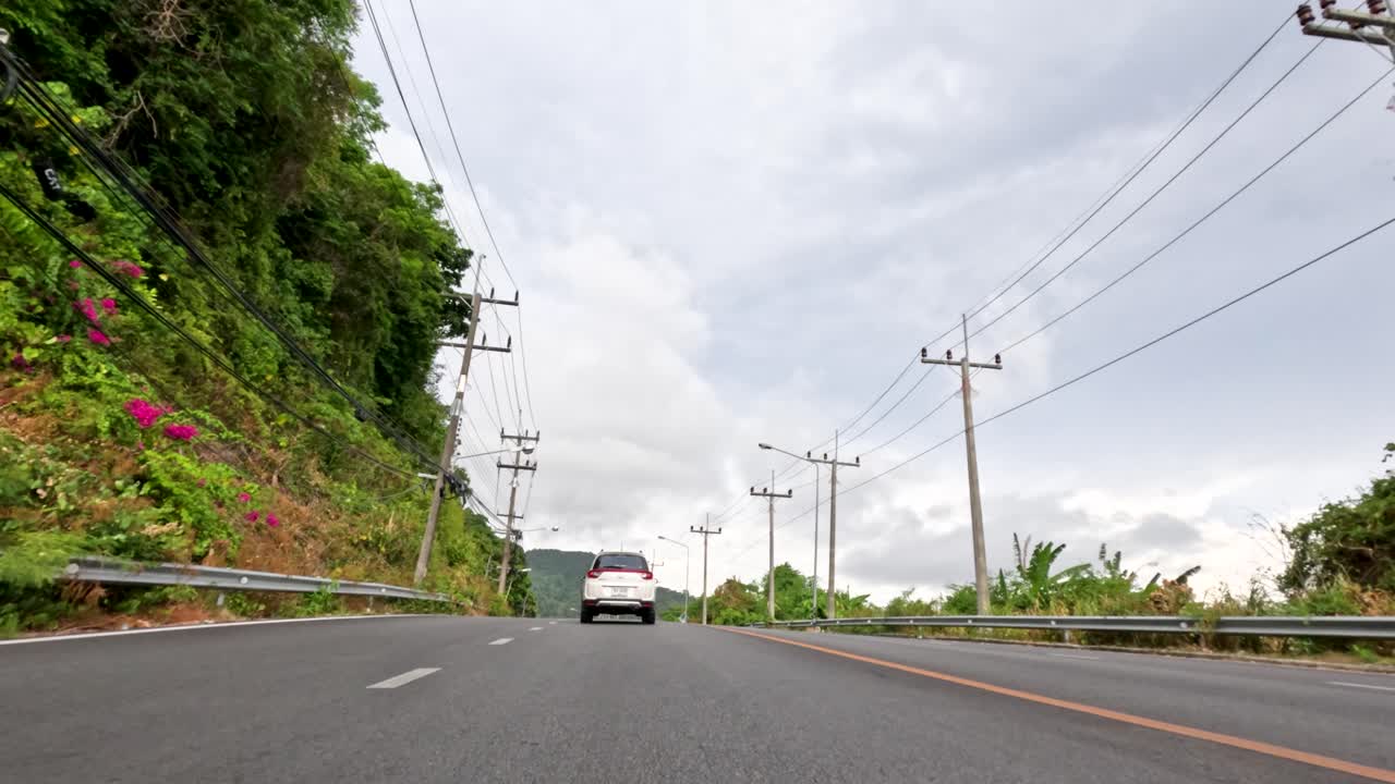 Vehicles travel on lush, winding road under overcast sky, low angle, smooth forward camera movement