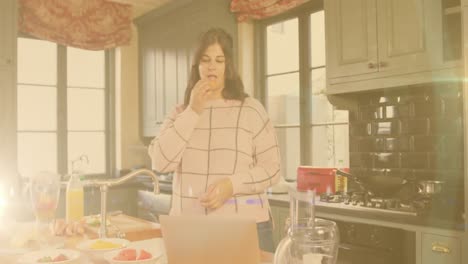 animación de luces parpadeantes sobre una mujer comiendo en la cocina usando una computadora portátil en la cocina en casa