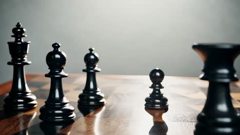 close up of black chess pieces on a wooden chessboard.