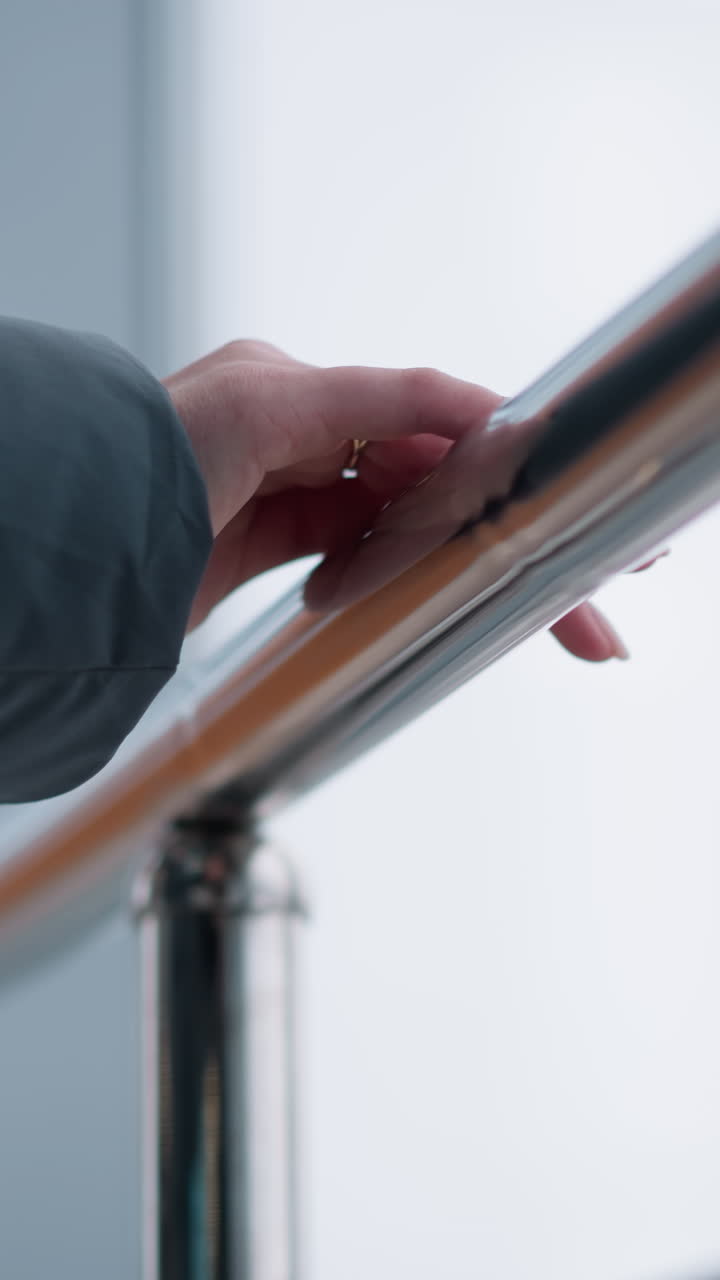 큰 유리 창문이 있는 현대적인 건물에서 는 동안 매끄러운 철도에서 미끄러지는 반지로 장식된 여성 손의 클로즈업