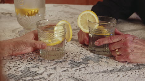 close up footage of showing only the hands of two elderly persons at a table with embroided table cloth each holding a glass of lemonade