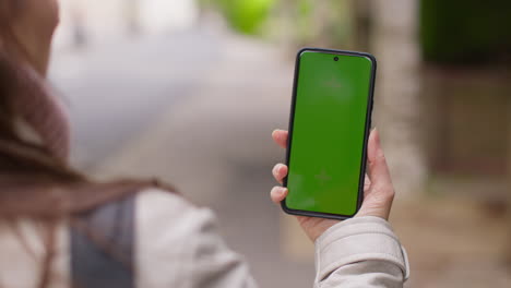 sobre el hombro disparo de cerca de la mujer al aire libre en la calle de la ciudad sosteniendo un teléfono móvil de pantalla verde