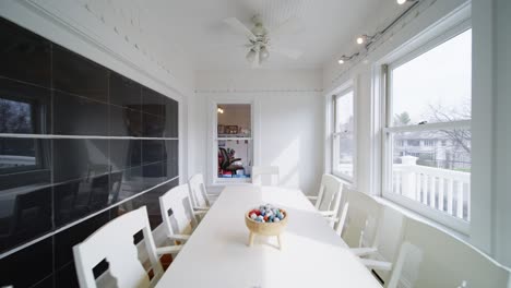 bright sunroom with a long white dining table and chairs, surrounded by windows letting in soft natural light