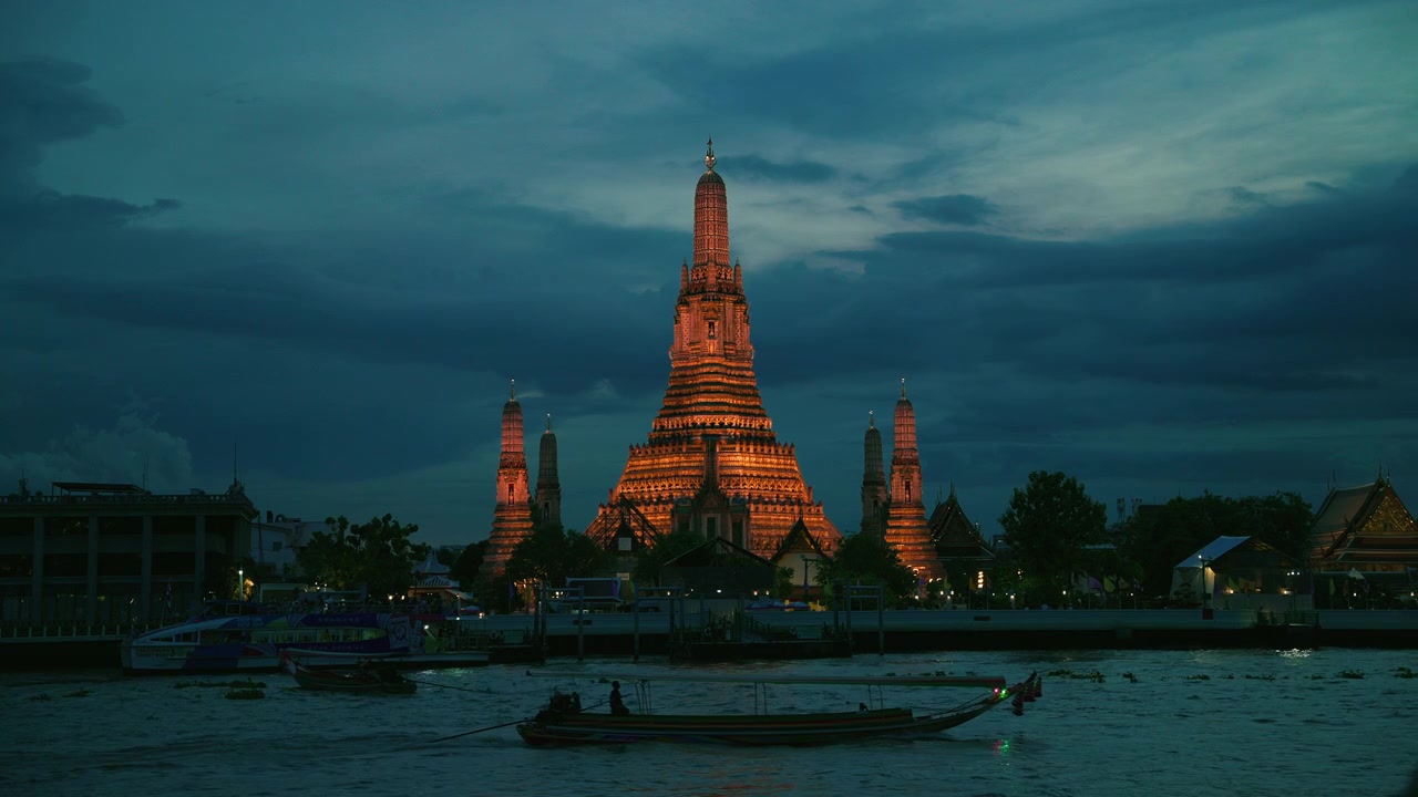 Il Tempio Wat Arun dell'Alba illuminato al crepuscolo, riflesso sul fiume Chao Phraya con una tradizionale barca a coda lunga, Bangkok, Thailandia. Ripresa statica 4K.