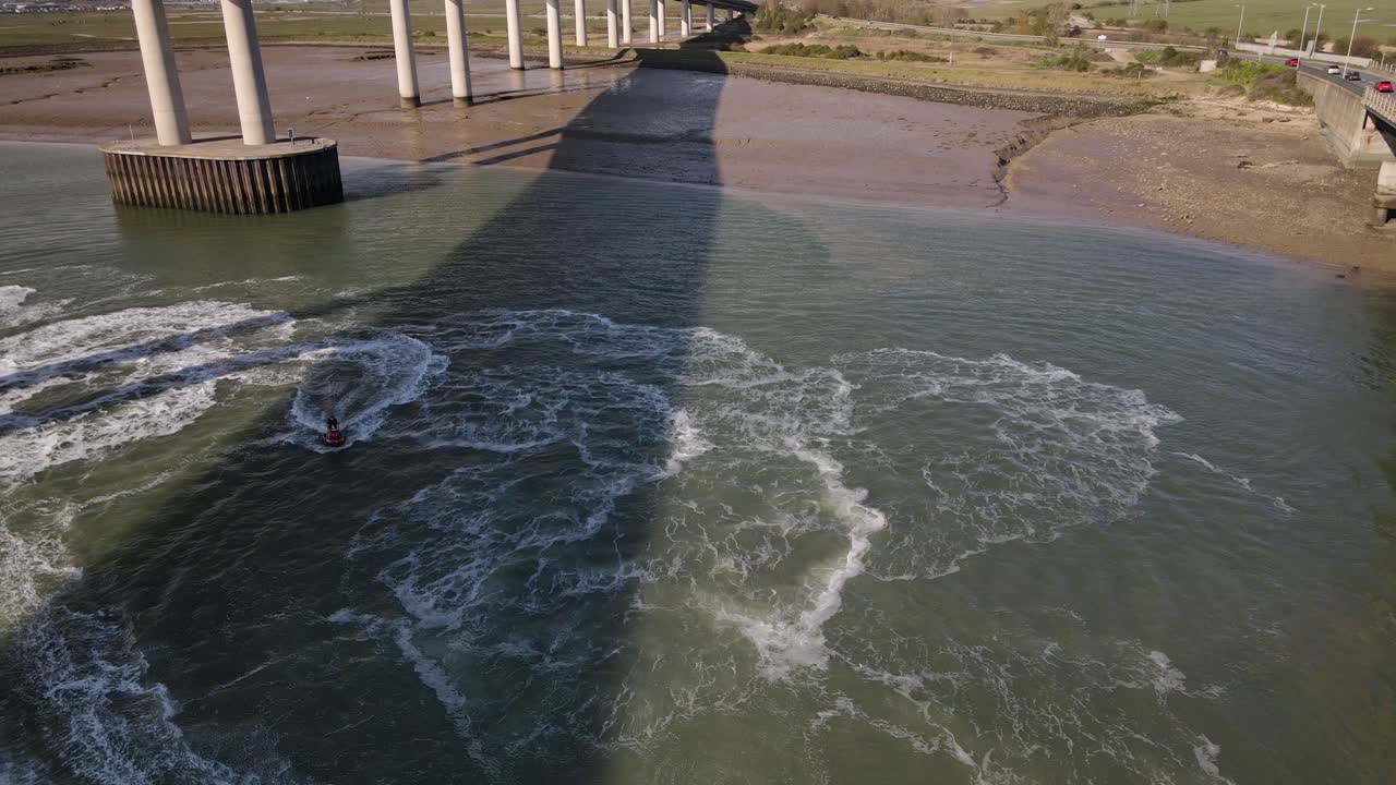 jet ski en el cenagal bajo el puente kingsferry y el puente de cruce sheppey en kent, inglaterra