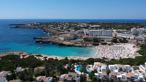 aerial shot of people on vacation on beautiful beach cove near holiday complex in menorca, spain