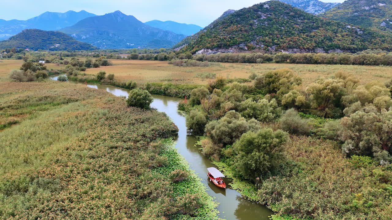 Ulcinj, Montenegro, 14 August 2025: River boat among lake reeds. A small wooden boat moves through dense green reeds toward the distant mountains