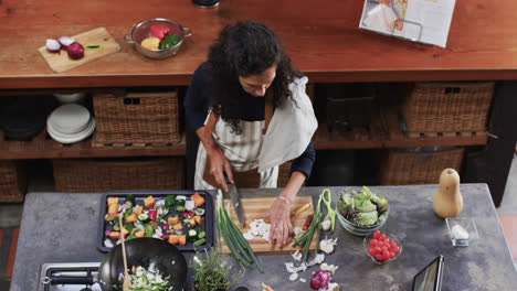 Biracial-woman-chopping-vegetables-using-tablet-in-kitchen,-slow-motion