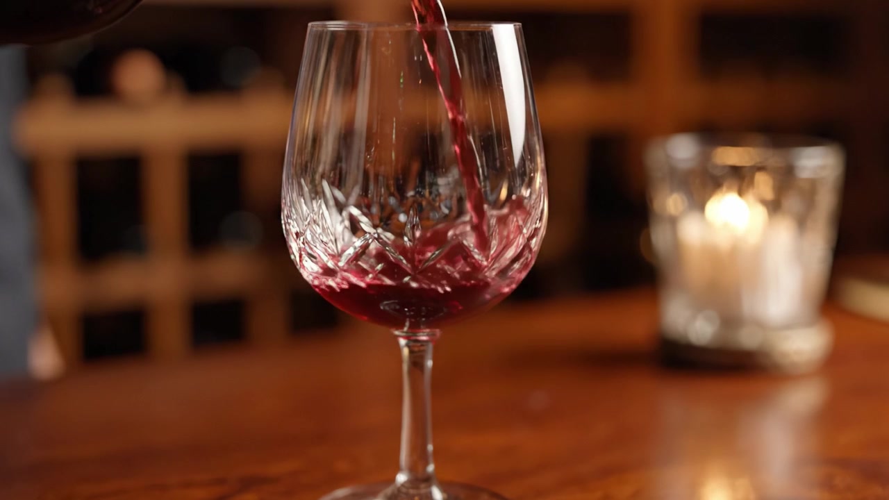 Elegante calice di cristallo che viene riempito con un ricco vino rosso, mostrando una mescita perfetta in un ambiente caldo e invitante che esalta la bellezza della buona cucina e del relax.
