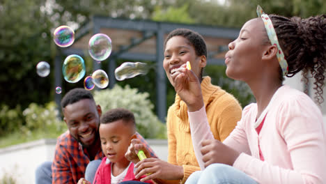 happy african american parents, son and daughter blowing bubbles in sunny garden