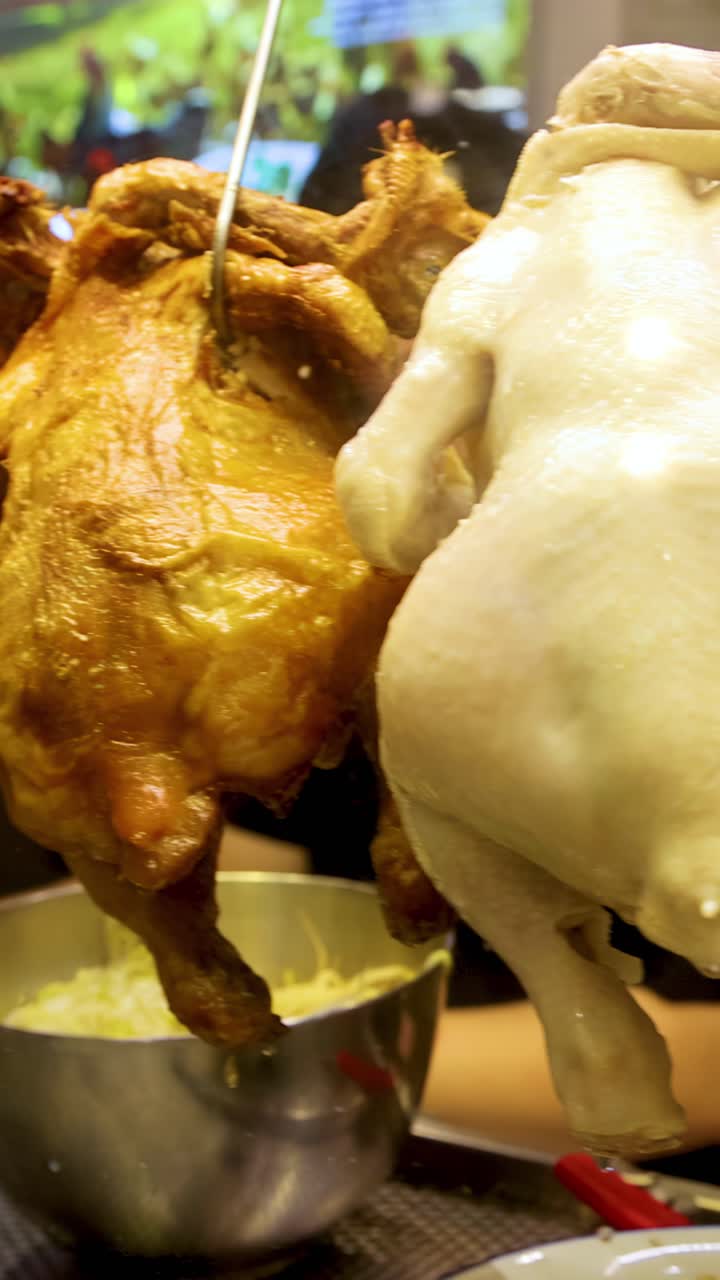 Un venditore di cibo sostituisce polli arrostiti con polli al vapore in una vetrina di vetro sotto un'illuminazione interna calda. La telecamera segue da vicino il movimento della mano