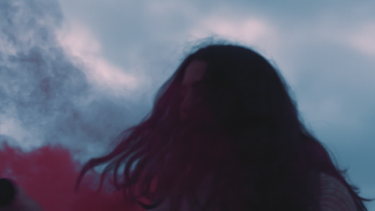 mujer joven jugando con granada de humo rosa bailando en la playa disfrutando de la libertad