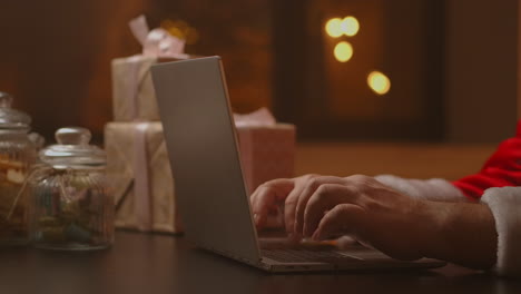 Las-Manos-De-Santa-Están-Escribiendo-En-El-Teclado-De-Una-Computadora-Portátil.-Papá-Noel-Está-Distribuyendo-Regalos-Para-Los-Niños-Buenos-Para-Navidad-Y-Año-Nuevo.-Imágenes-4k-De-Alta-Calidad