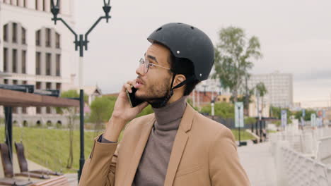 Young-American-Man-In-Formal-Clothes-And-Helmet-Having-A-Call-On-Mobile-Phone-While-Sitting-On-Bike-In-The-City-1