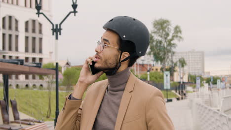 young american man in formal clothes and helmet having a call on mobile phone while sitting on bike in the city 1