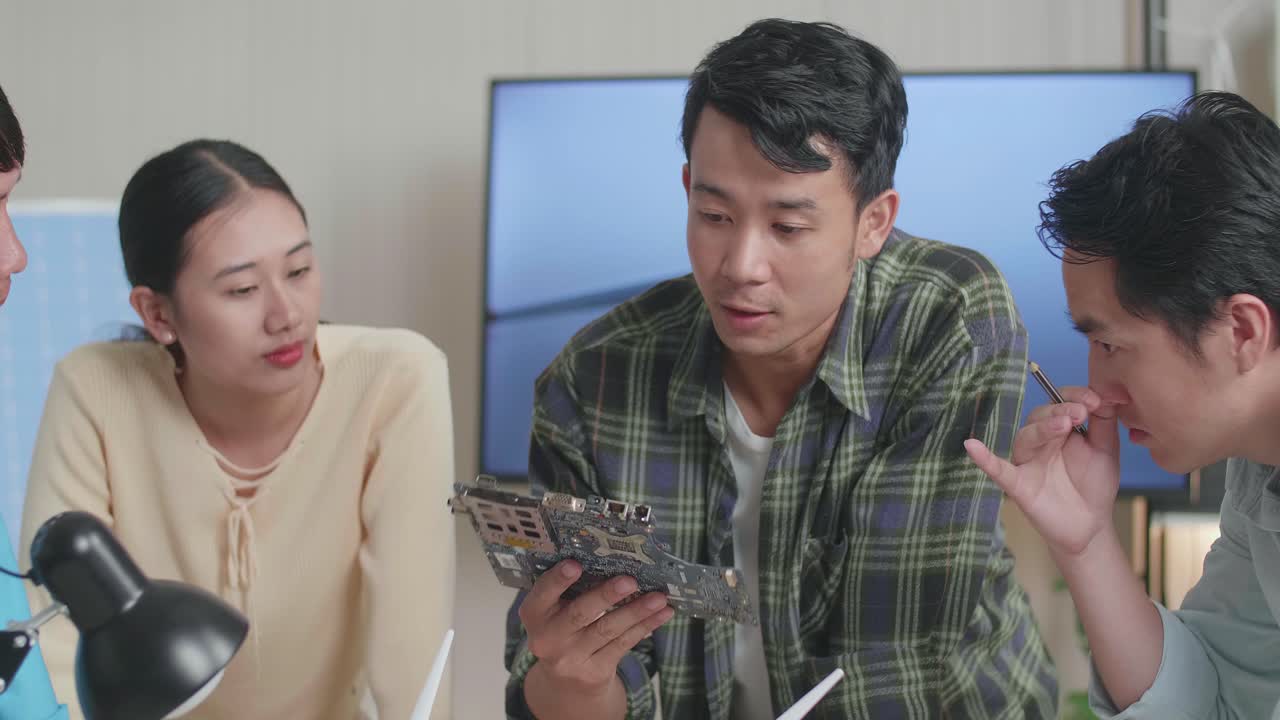 풍력 터빈을 가진 아시아 엔지니어 그룹이 사무실에서 녹색 회로 보드에 대한 회의를 하고 있습니다.