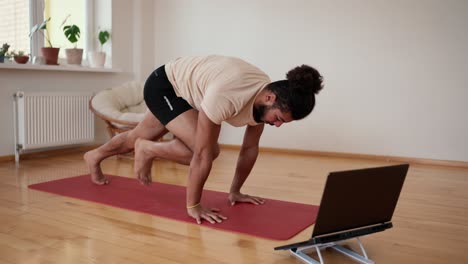 Hombre-Atlético-De-Raza-Mixta-En-Forma-Viendo-Clases-De-Entrenamiento-En-Línea-En-Una-Computadora-Portátil,-Repitiendo-Movimientos-Después-Del-Instructor