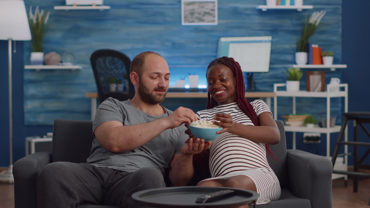 POV of interracial couple with pregnancy watching television