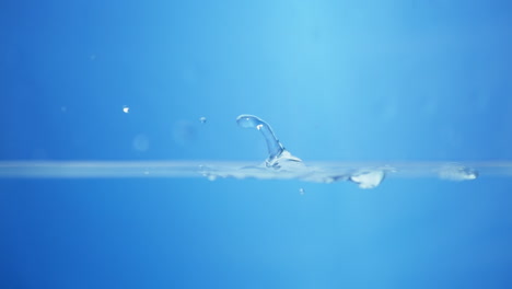 salpicaduras de agua que crean pequeñas gotas y ondas en un recipiente lleno de agua contra un fondo azul