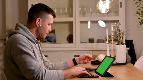 Diligent-white-young-professional-inputs-credit-card-information-on-tablet-computer,-concentrated-on-task-with-a-focused-expression-while-seated-at-table