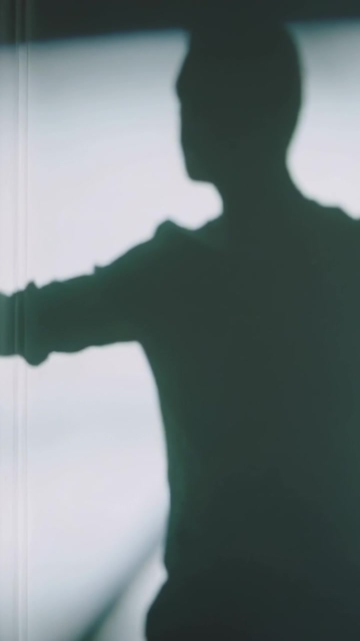 Vertical video: Framing male figure moving left reach to neck stretch by bright window long sleeves