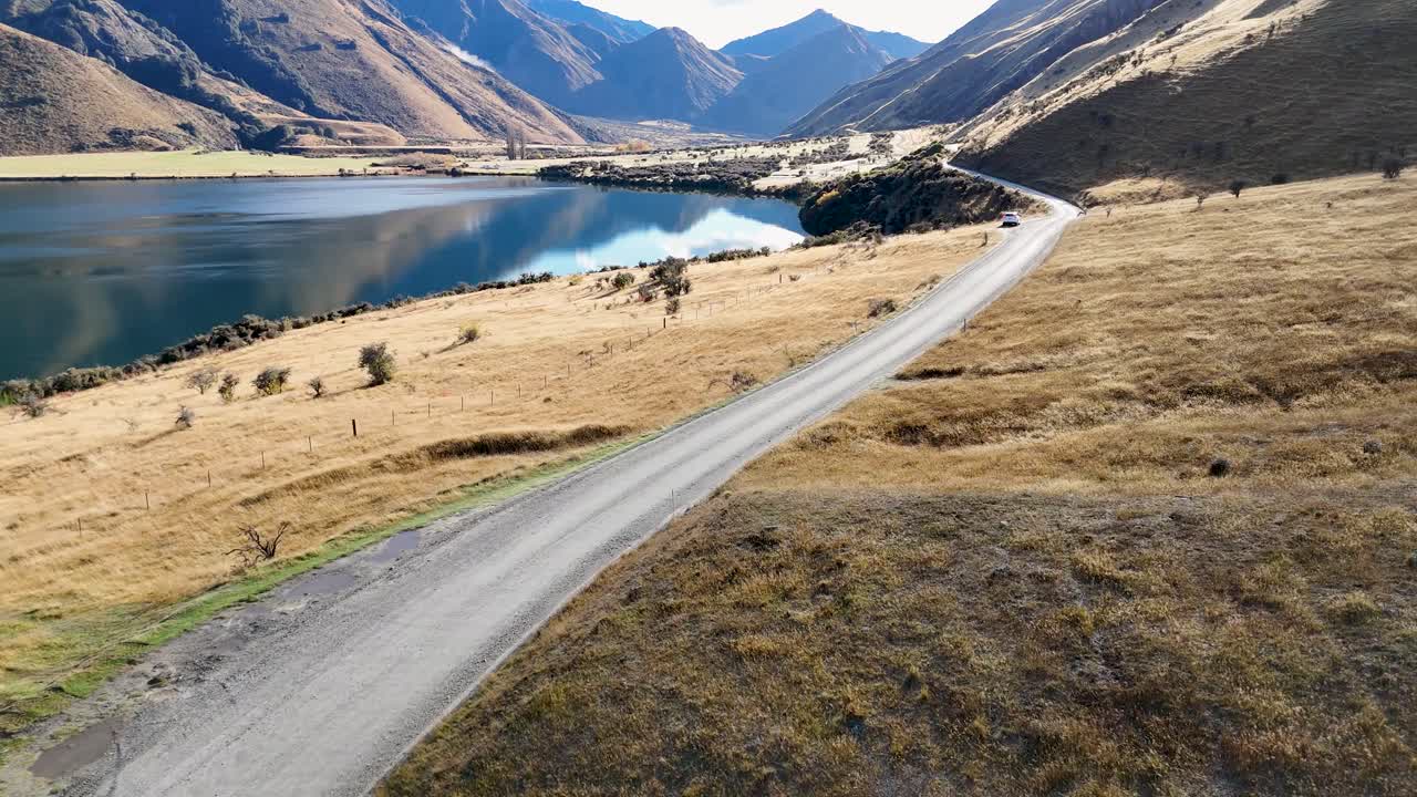 Aerial view of a winding road beside Lake Moke, surrounded by mountains under clear skies in Queenstown, New Zealand