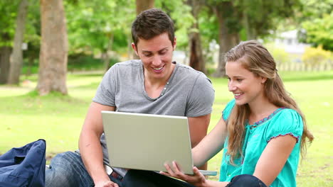 Two-friends-laughing-and-talking-while-looking-at-a-laptop-as-they-sit-in-a-park