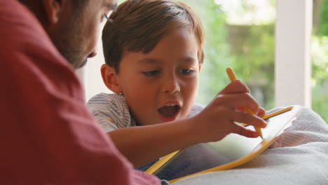 padre e hijo en casa en el sofá en la sala de estar jugando con el juego de dibujo juntos