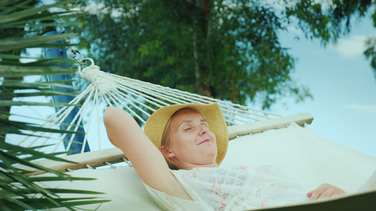 한 젊은 여성이 해먹에서 휴가를 즐기는 해변 휴양지에서 쉬고 있다