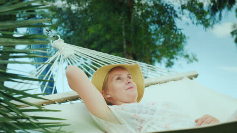 a young woman is resting in a seaside resort in a hammock enjoying a vacation