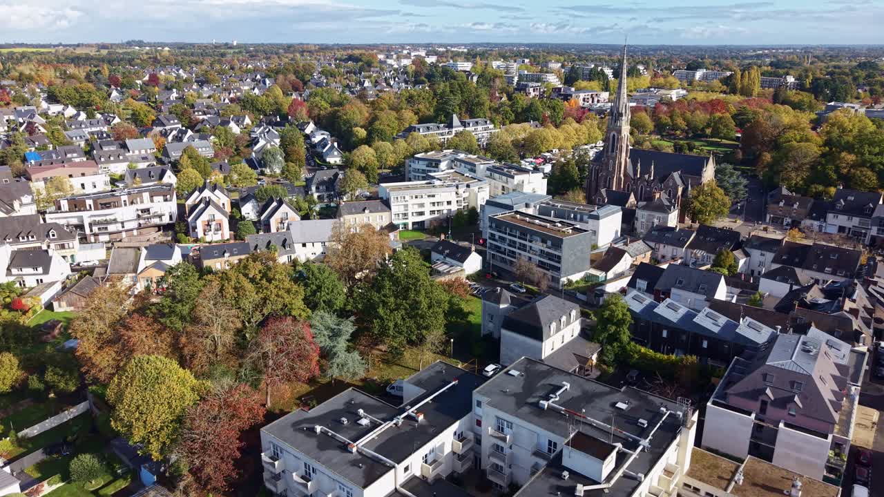 Drone shot flying forward above Cesson-Sévigné, France, showing Saint-Martin Church, residential buildings, trees, and streets on a clear sunny day