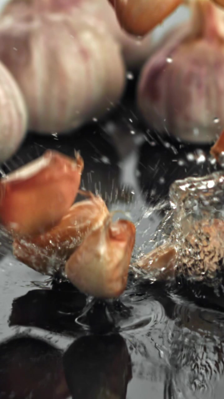 Fresh Garlic Cloves Splashing into Water on a Dark Surface