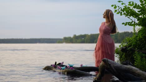 Eine-Wunderschöne-Blonde-Frau,-Die-Ein-Rosa-Kleid-Im-Wasser-Neben-Kerzen-Und-Blumen-Trägt