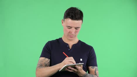 잘생긴 젊은 남자의 초상화는 노트북에 연필로 쓰고 생각하고 계속 쓰고 있습니다. 녹색 화면