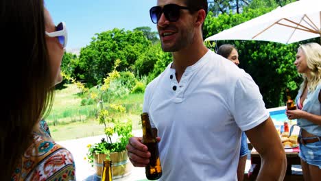 Pareja-Interactuando-Mientras-Toma-Una-Botella-De-Cerveza-Cerca-De-La-Piscina