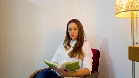 Mujer-Leyendo-Un-Libro-Por-La-Noche-Después-Del-Trabajo-Sentada-En-Un-Sillón-Rojo