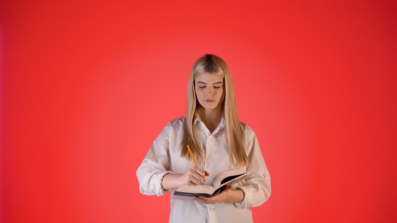 joven rubia usando borrador de lápiz luego pensando, fotografía de estudio con fondo rojo